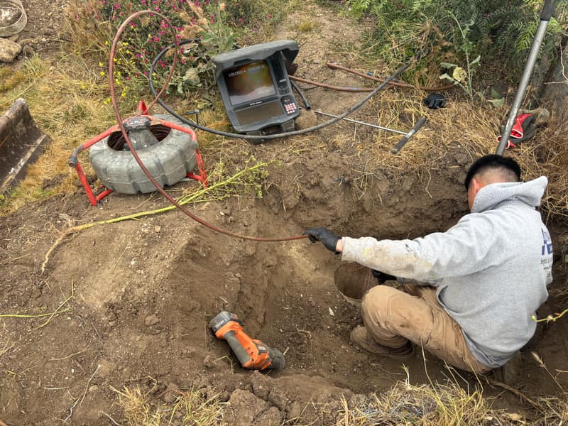Technician feeding an inspection camera into an exposed septic line in a trench