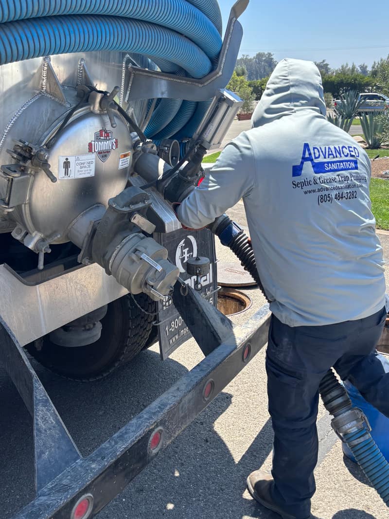 Technician connecting a large vacuum hose to the valve on a chrome pump truck tank