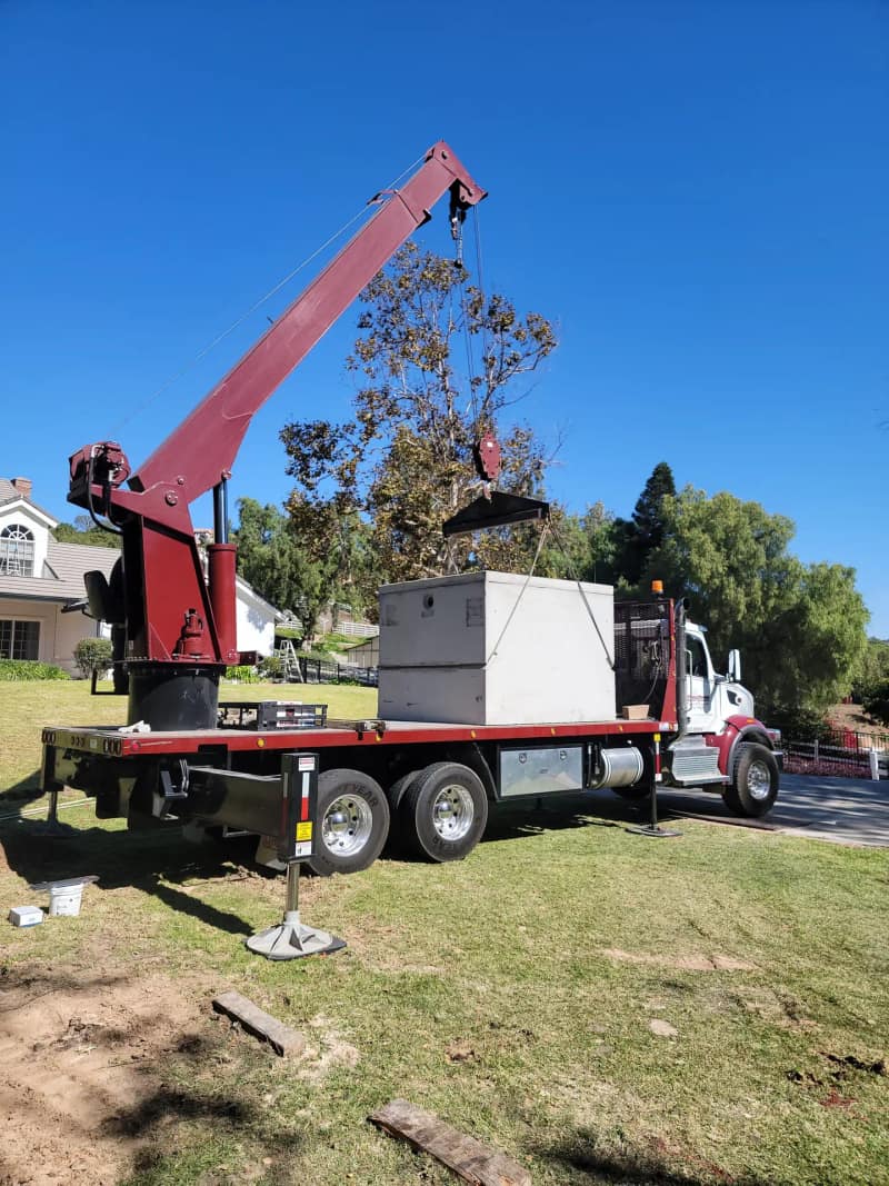 Boom truck lowering a concrete septic tank into place on a residential lot