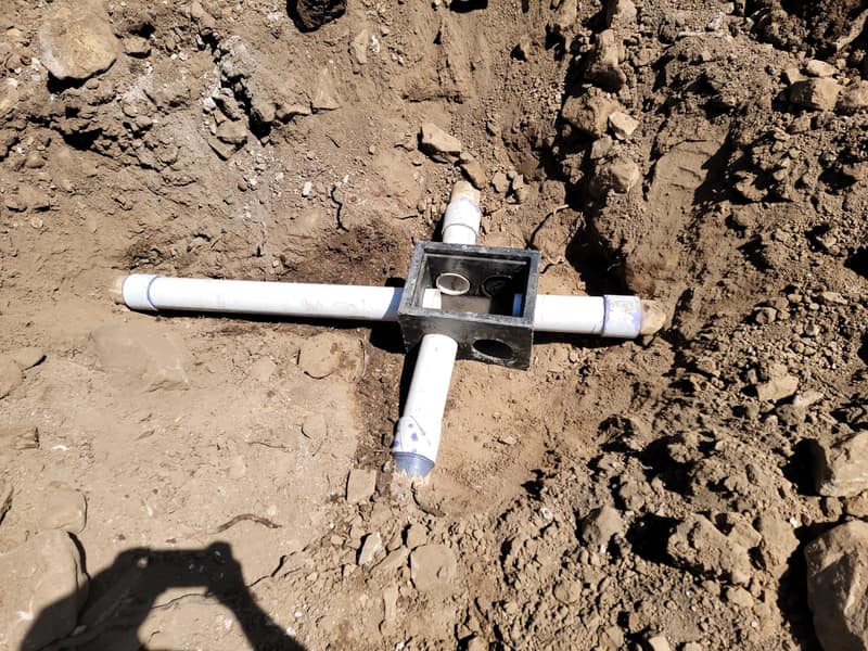 White PVC pipe and fittings laid in an open trench during a septic installation