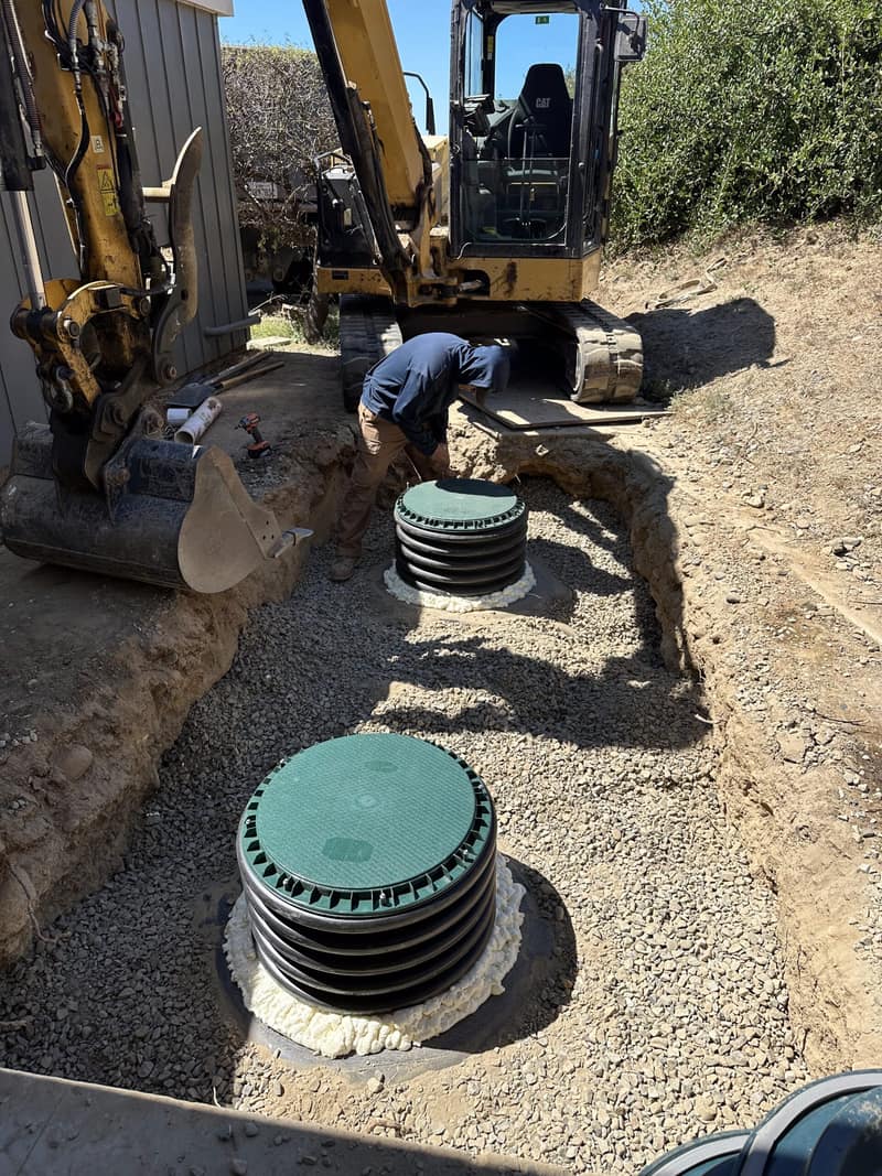 Excavator beside a new septic tank with risers set in a gravel bed