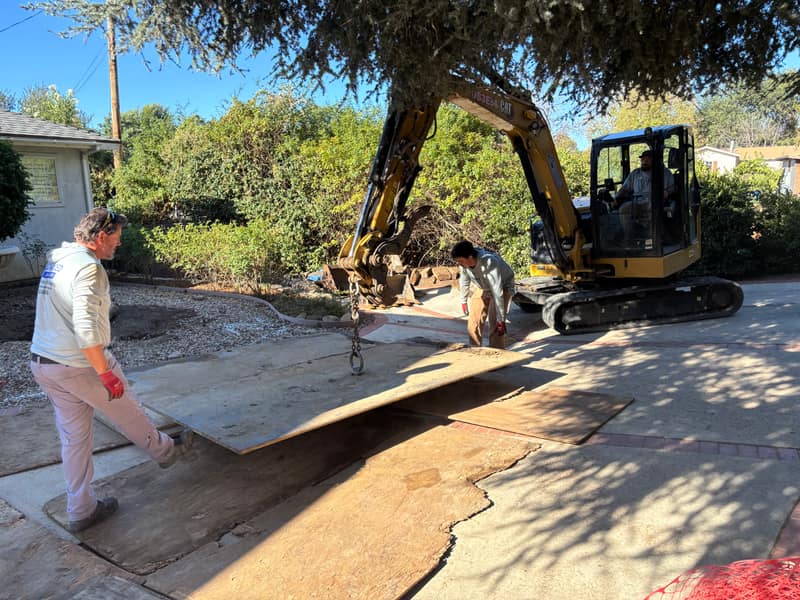 Crew member placing a protective ground mat across a yard ahead of an excavator
