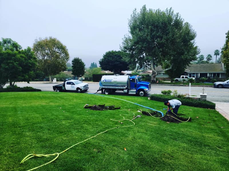 Pump truck at the curb with a hose running across a front lawn to the tank