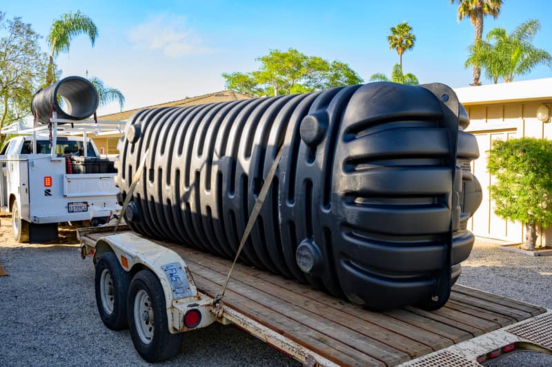 New black Roth multi-layer septic tank strapped to a trailer outside a home