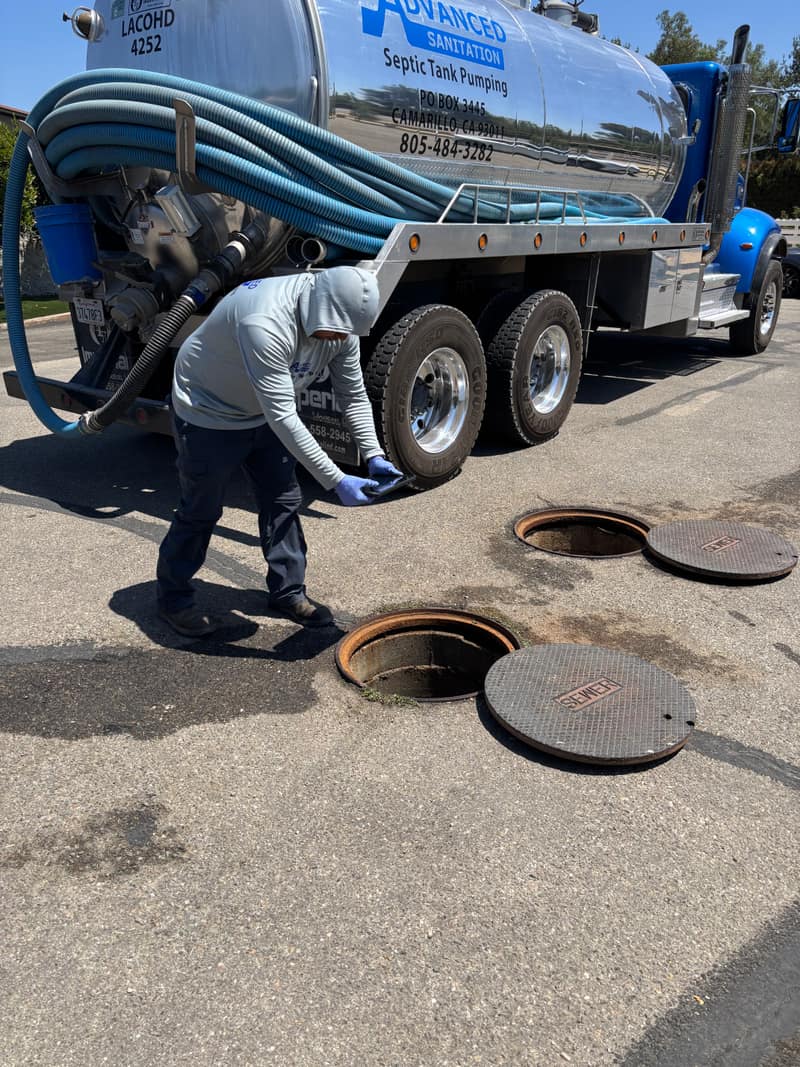 Technician checking an open septic tank beside a pump truck in a residential driveway