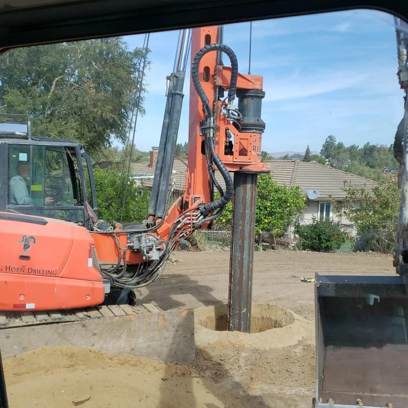 Orange drill rig with its auger set into a freshly started seepage pit hole