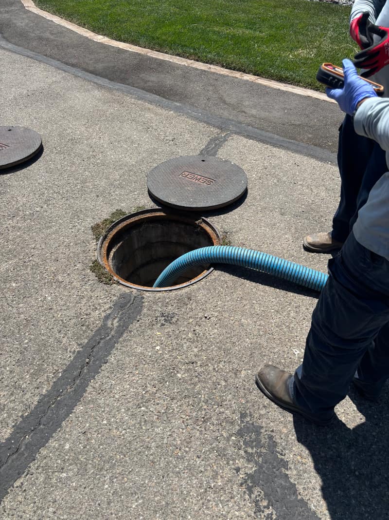 Technician guiding a vacuum hose into an open septic tank lid on a paved driveway