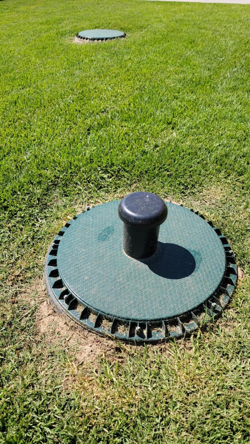 Green septic riser lid with an air filter vent sitting flush in a mowed lawn