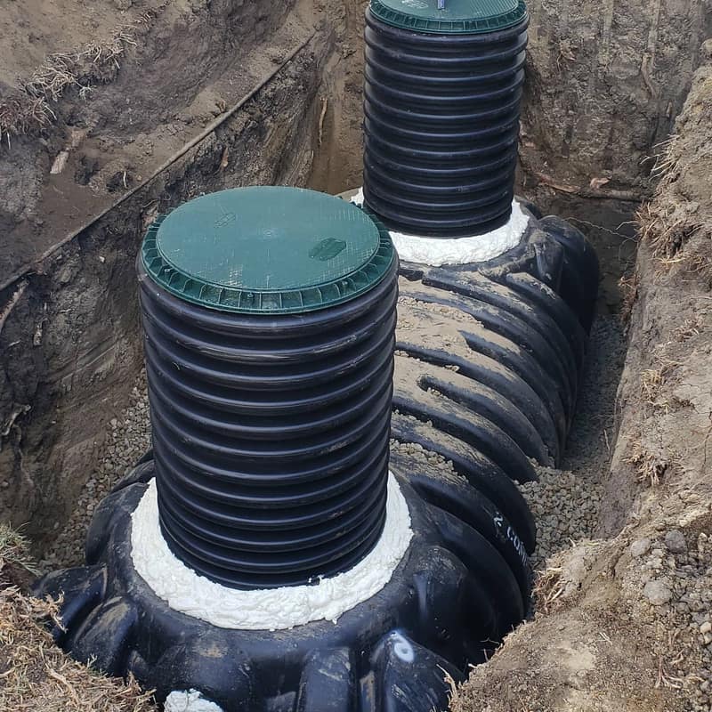 Two green-lidded plastic risers installed on a new septic tank before backfill