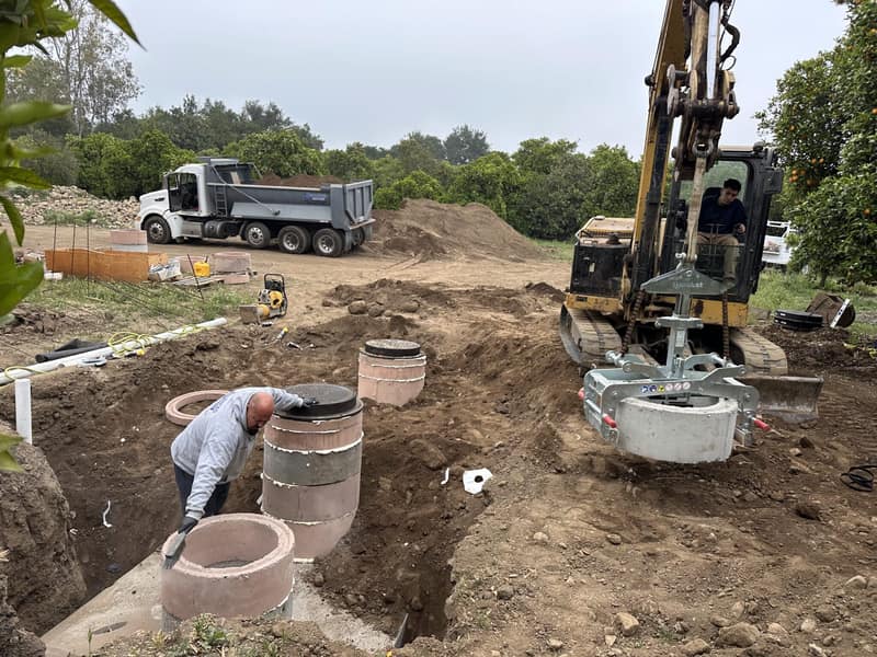 Concrete traffic-rated risers being set over a septic tank during excavation