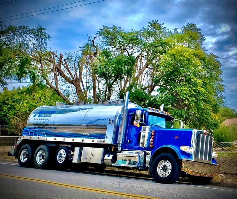 Blue Peterbilt pump truck with a polished chrome tank under a dramatic sky