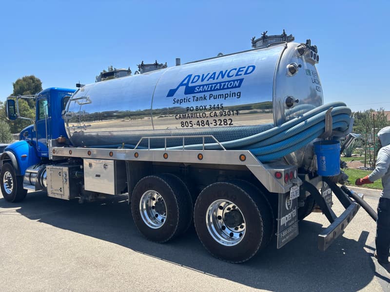 Advanced Sanitation pump truck with a blue cab, polished chrome tank and coiled vacuum hoses at a customer's street