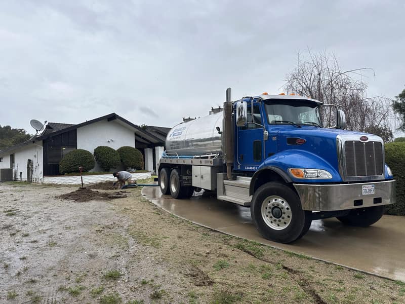 Blue Advanced Sanitation pump truck in a home's driveway while a technician works at the open tank