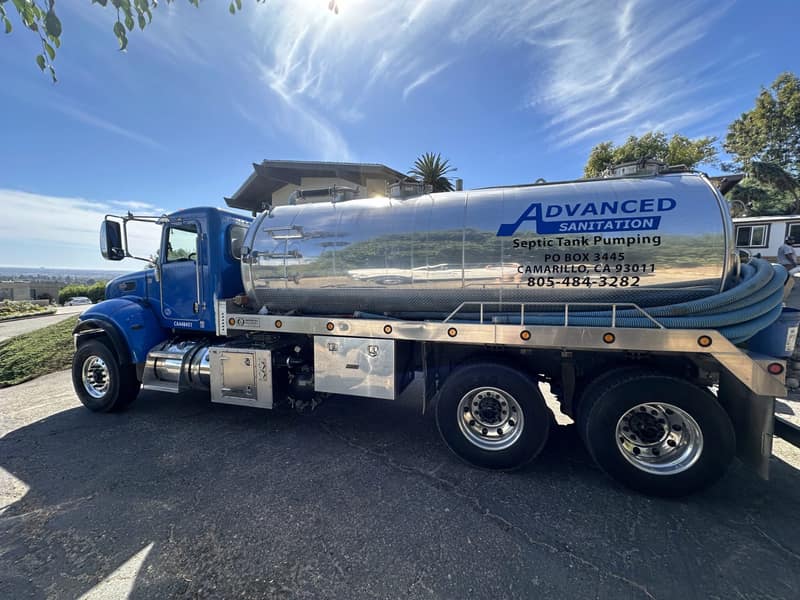 Advanced Sanitation pump truck with a blue cab and chrome tank on a hillside road